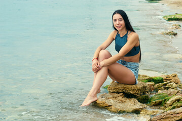 A young beautiful girl in shorts is sitting on a rocky shore