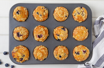 Ready lemon muffins with blueberries and shtreisel in baking form on a white wooden background....
