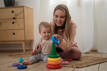 Mother playing with her cute baby child pyramid game at home. Portrait of professional nanny...