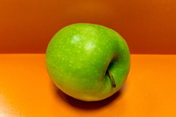 Juicy green apple on an orange background. A ripe green apple lies on its side