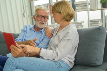 Obraz premium Senior caucasian couple using tablet sitting on sofa