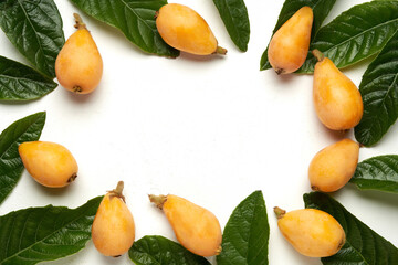 Frame made of fresh organic loquat fruits with green leaves on white background. Flat lay, top view, copy space