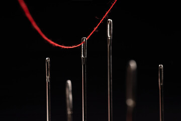 Red thread passing through needles on a black background