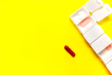 White weekly pillbox with different tablets of colors isolate on yellow background with big copy...