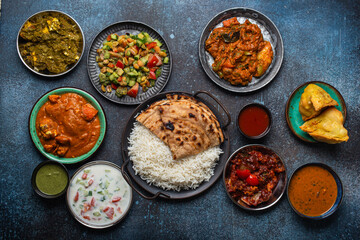 Assorted Indian ethnic food buffet on rustic concrete table from above: curry, fried samosa, rice...