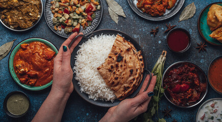 Assorted Indian ethnic food buffet on rustic concrete table from above: curry, fried samosa, rice...