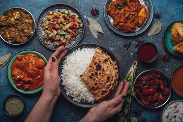 Assorted Indian ethnic food buffet on rustic concrete table from above: curry, fried samosa, rice biryani, dal, paneer, chapatti, naan, chicken tikka masala, traditional dishes of India for dinner