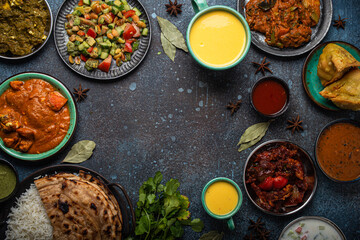 Indian ethnic food buffet on concrete table from above: curry, samosa, rice biryani, dal, paneer, chapatti, naan, chicken tikka masala, mango lassi, dishes of India for dinner background copy space
