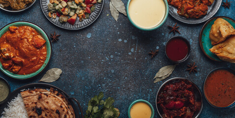 Indian ethnic food buffet on concrete table from above: curry, samosa, rice biryani, dal, paneer, chapatti, naan, chicken tikka masala, mango lassi, dishes of India for dinner background copy space