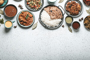 Indian ethnic food buffet on white concrete table top view: curry, samosa, rice biryani, dal, paneer, chapatti, naan, chicken tikka masala, mango lassi, dishes of India dinner background copy space