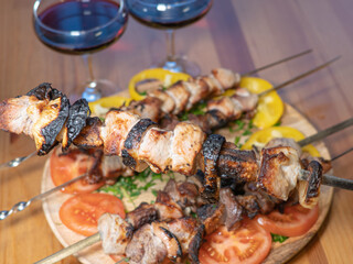 meat on skewers, pieces of fried pork, barbecue. Dish with vegetables and glasses with red wine
