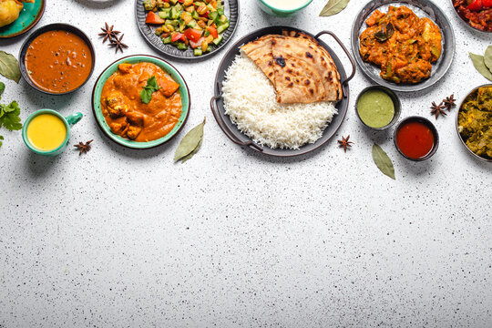 Indian ethnic food buffet on white concrete table top view: curry, samosa, rice biryani, dal, paneer, chapatti, naan, chicken tikka masala, mango lassi, dishes of India dinner background copy space