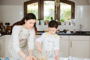 Obraz na płótnie Canvas Mother with child bake muffins together in the kitchen, at home. White kitchen. Mom spends time with her son. 
