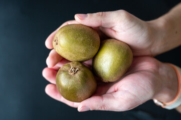 Hands holding three kiwi on dark background