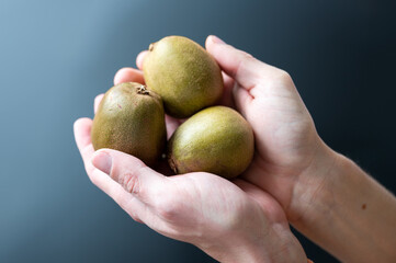 Hands holding three kiwi on dark background