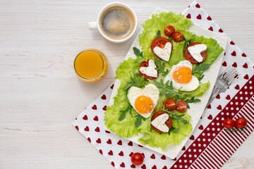Breakfast on Valentines Day breakfast for two with heart-shaped eggs vegetables and cheese with coffee and juice on a white wooden table covered with a beautiful napkin. Healthy breakfast. Top view