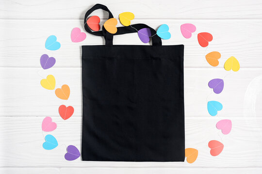 Valentines mockup black tote bag with paper colorful hearts on white wooden background, flat lay, top view, copy space.