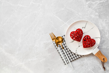 Banner. Table setting. A fashionable marble plate with a napkin, fork and red hearts on a gray background. Valentine's Day holiday concept for cafes and restaurants. A copy of the place for the text.