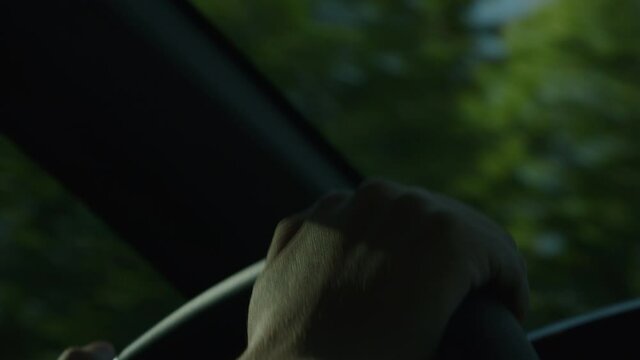 Hand holding a steering wheel of a car while driving in the forest and sunbeams and light rays hit the woman's hand as they sift through the trees, concept of freedom, road safety, attentive driving