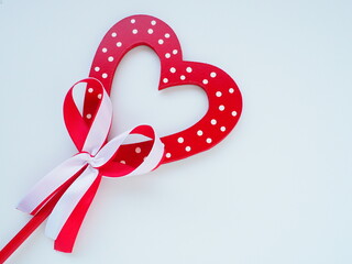 Valentine's day concept. Red wooden heart with white dots and ribbon bow on a stick. White...