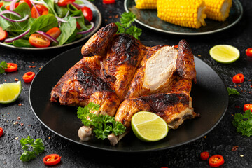 Roast Chicken Tabaka with salad, corn and lime on black plate.