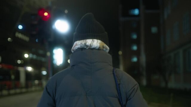 Cinematic and real scene of a person in packed winter clothes walking across a crosswalk in a urban street while bus goes by, green light blinking in downtown, cold winter night