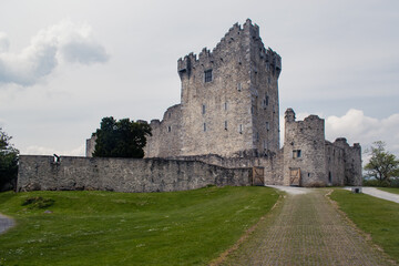 Fototapeta na wymiar Old stone brick medieval castle with grey cloudy sky and green grass 