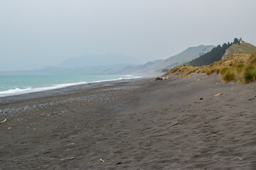 White waves crashing on black sand beach with misty mountains and foggy sky 