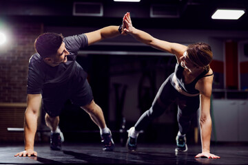 Fototapeta A fit sporty couple giving high five to each other while doing planks and exercises in a gym. obraz