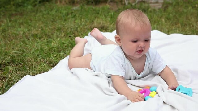 Little newborn girl lying on tummy chewing rattle on blanket, summer day outdoor. Infant having fun outdoors. Infant baby child resting playing learning to crawl. Motherhood teething, babyhood concept