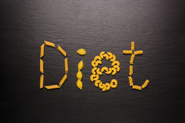 word DIET made of variety of pasta, on a black slate background, diet and food concept, flat lay