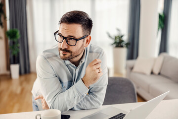 A man with eyeglasses thinking while leaning on kitchen counter at his cozy home.