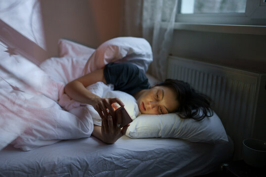 Social media jealousy. Young depressed woman addicted to mobile phone lying in bed at home, scrolling social media, feeling envious of lives of others, reading what people posting and sharing online