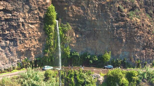 Aerial 4K footage of a drone flight over Angels waterfall (Cascata dos Anjos) in Madeira island. The waterfall cascades over the rockface onto the regional roadway, and spills into the sea below