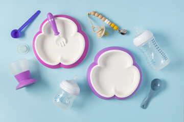 Top view set of plastic dishware, feeding bottles and pacifier on blue background, flat lay