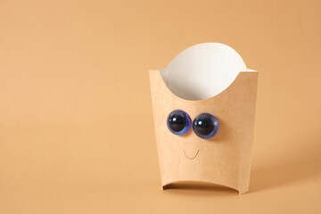 cardboard packaging for fries or other fast food product with doll eyes on a light brown background