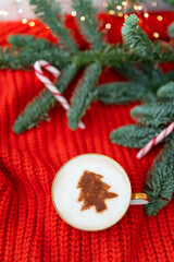 Christmas composition made of Norwegian Nobilis pine and decorated with lights and candy canes in the form of a cane. A cup of cappuccino with a Christmas tree pattern. Christmas and New Year concept.