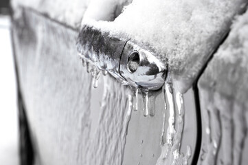 Closeup view of car door handle and lock covered in ice during winter storm. 