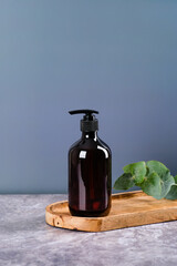 Dark brown amber glass dispenser bottle with shower gel o, eucalyptus leaves on wooden board. SPA natural beauty product design
