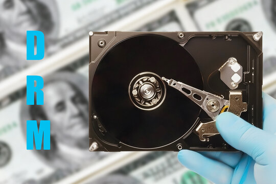 person holds computer hard drive with the abbreviation (drm) digital rights management on blurry background of dollar bills, concept of copyright protection