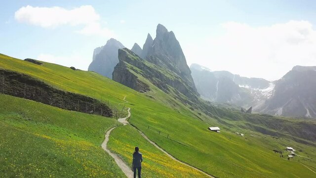 Aerial flight above woman hiking along trail path in alpine mountain peak in dolomites seceda sunny day