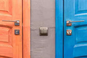 Orange and blue wooden door with iron handle and light switch next to part or element of the interior in the toilet