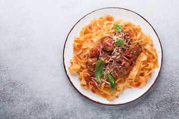 Tagliatelle pasta with meatballs in tomato sauce and thyme in sauce on light grey slate, stone or concrete background. Traditional Italian dish and cuisine. Top view with copy space.