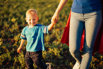 Super mom and her son walk forward holding hands. Cheerful family, a woman in a red raincoat as a...