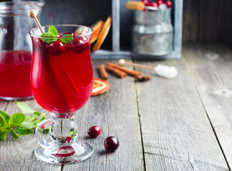 Fresh cranberry juice with cinnamon and anise in glass jars on the old wooden background. Selective focus.