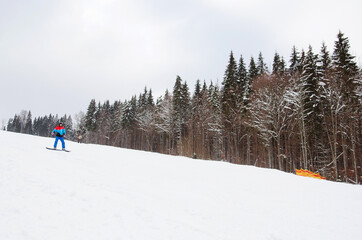 A male snowboarder descends the track next to a snowy forest. ski resort. Winter sport