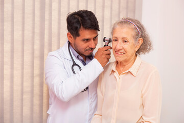 Doctor examining ear of elderly female with otoscope in clinic