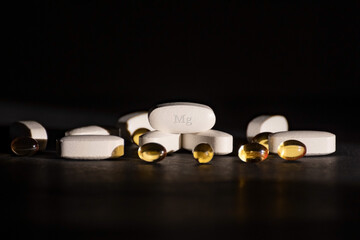 A complex of Mg ( magnesium, magnesium ) and vitamin D ( omega 3 ) capsules for the treatment and health of humans on a dark background. Copy space. - obrazy, fototapety, plakaty