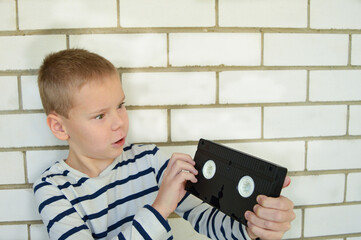 A boy on the background of a brick wall is holding a videotape, a very popular technology of the...
