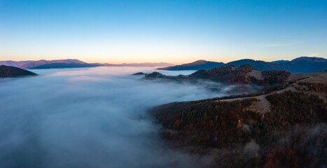 Fototapeta na wymiar Thick fog among peaks of high autumn mountains at sunrise